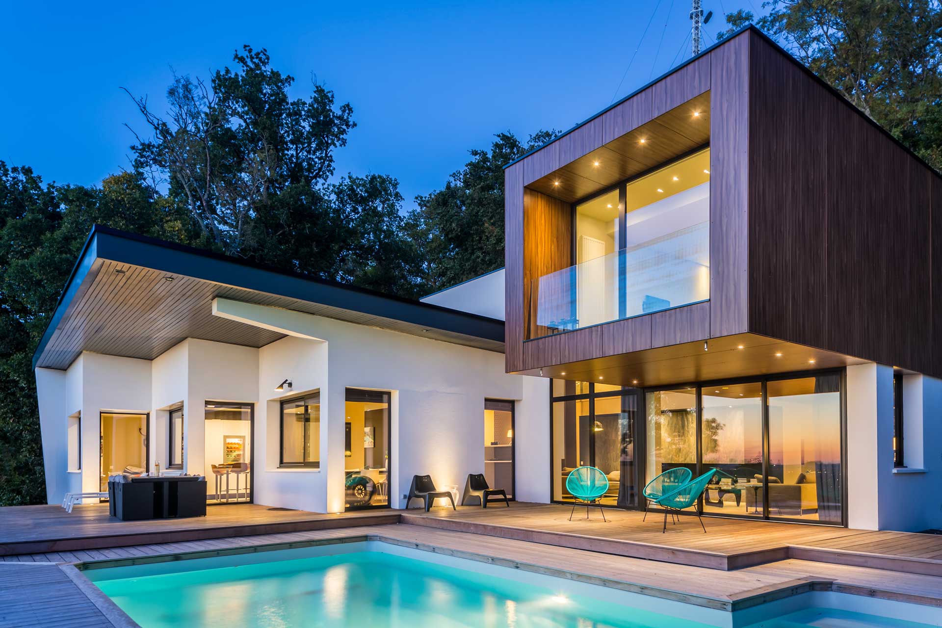 Maison contemporaine et sa piscine au crépuscule, façades éclairées