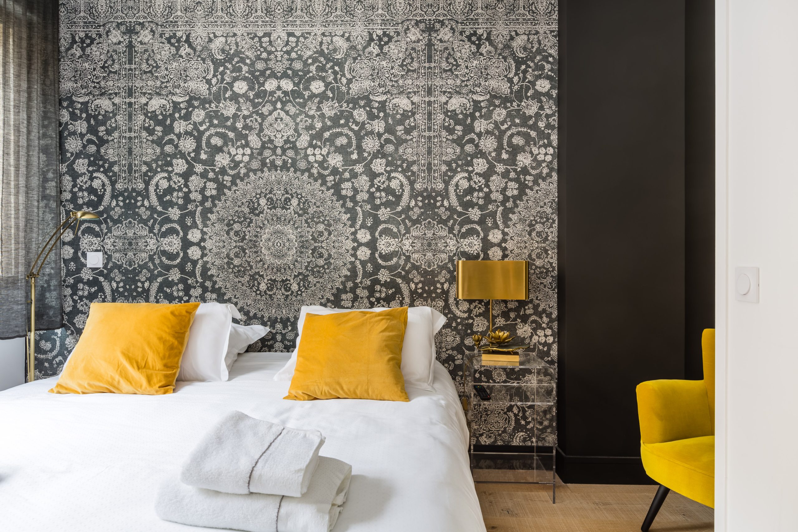 Chambre aux coussins jaunes et serviettes pliées sur le lit, papier peint à motifs
