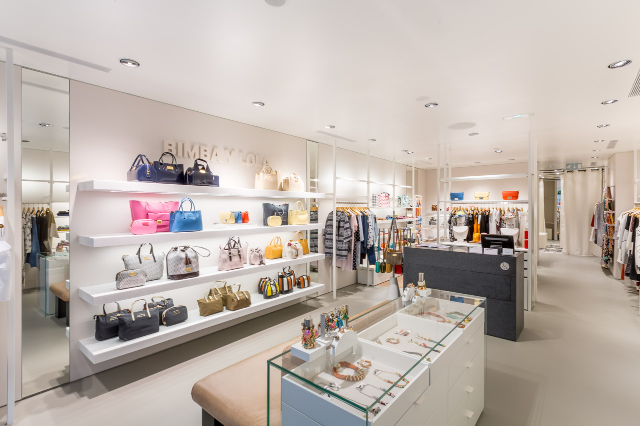 Boutique : étagères garnies de sacs, vitrines à bijoux et portants de vêtements