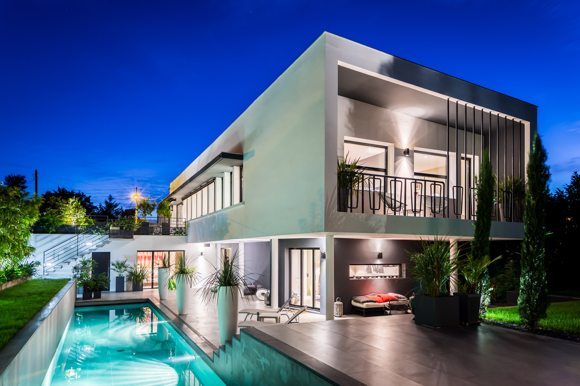 Maison contemporaine à l’heure bleue, volume en porte-à-faux au-dessus de la terrasse, piscine éclairée au premier plan