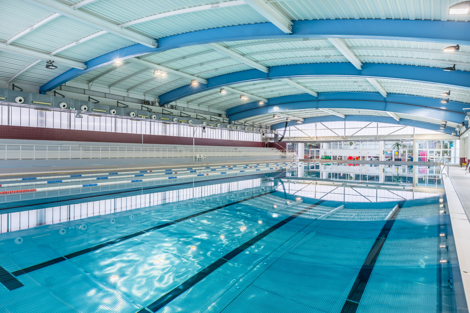 Piscine couverte sous une charpente métallique en arcs, bassin et lignes d’eau