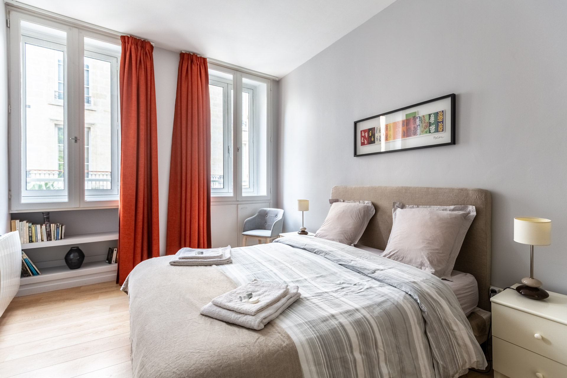 Chambre claire aux rideaux rouges et grandes fenêtres, serviettes posées sur le lit