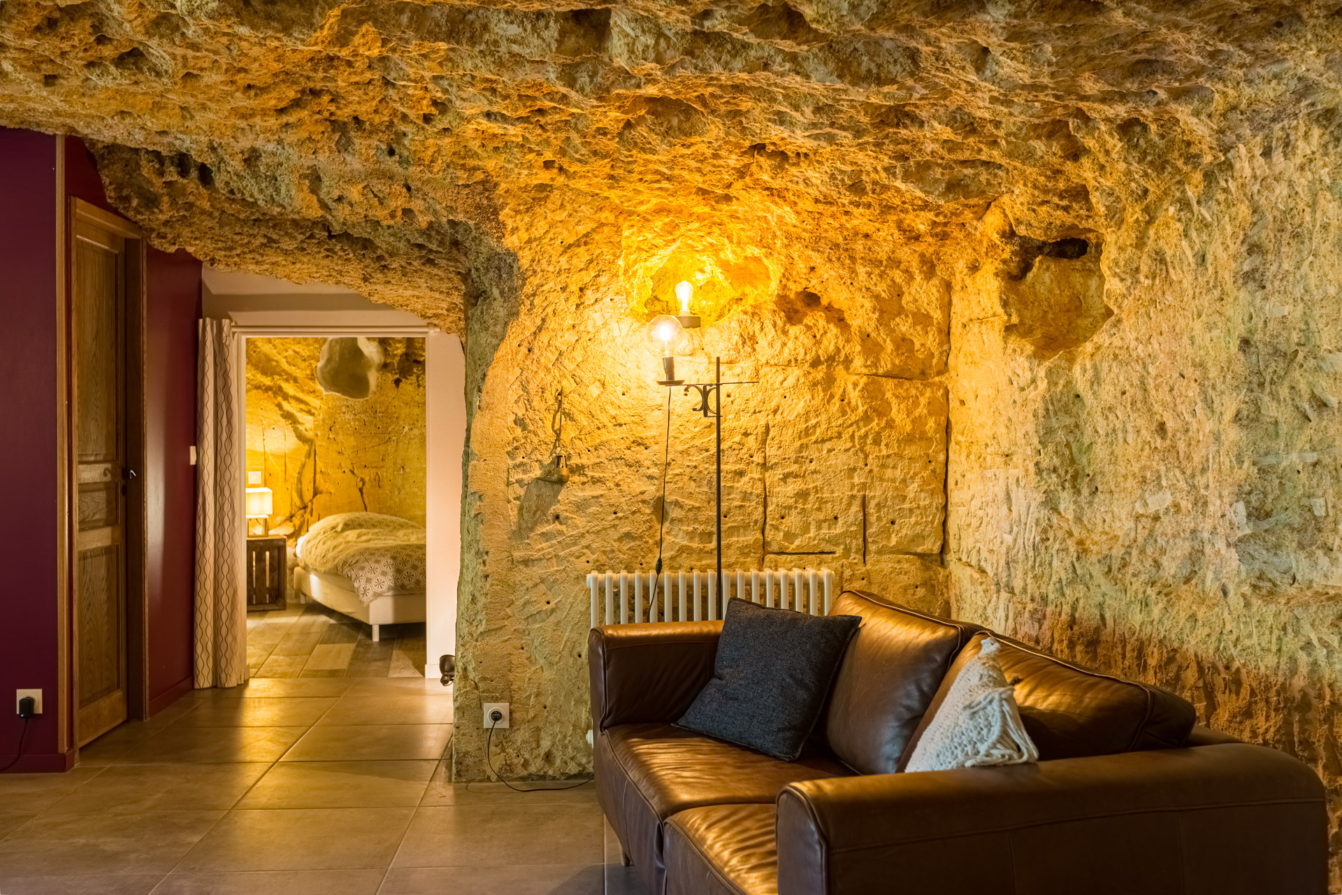 Salon troglodyte creusé dans la roche calcaire, canapé de cuir, chambre visible au fond