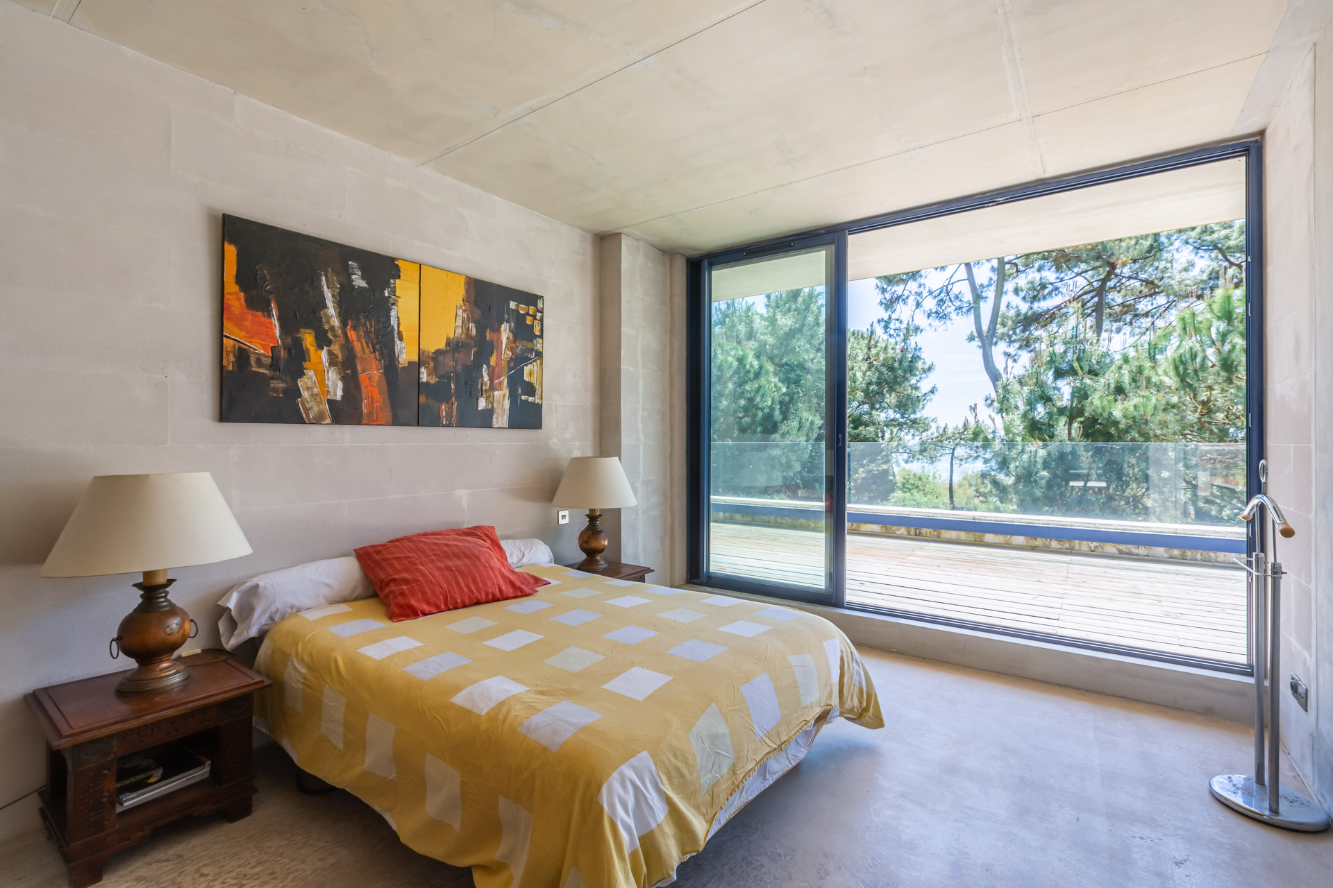 Chambre ouverte par une grande baie sur une terrasse et les pins