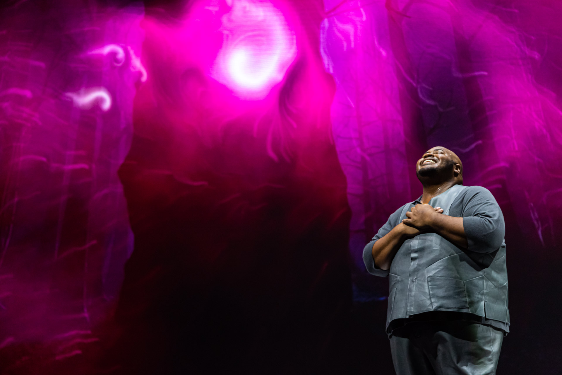 Un chanteur sous des lumières magenta, les mains sur la poitrine